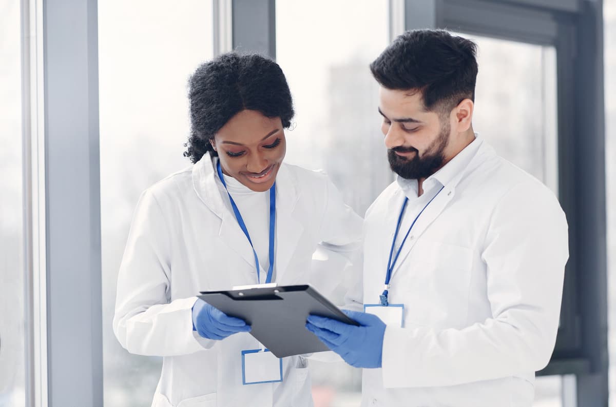 Two semiconductor engineers in cleanroom suits examining a silicon wafer at a fabrication workstation